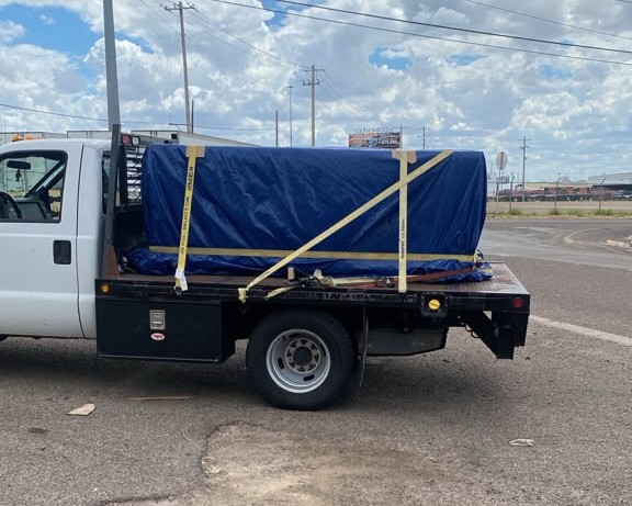 Flatbed truck carrying cargo covered with a blue tarp and secured with yellow straps during a ZALO Group cargo-handling operation.